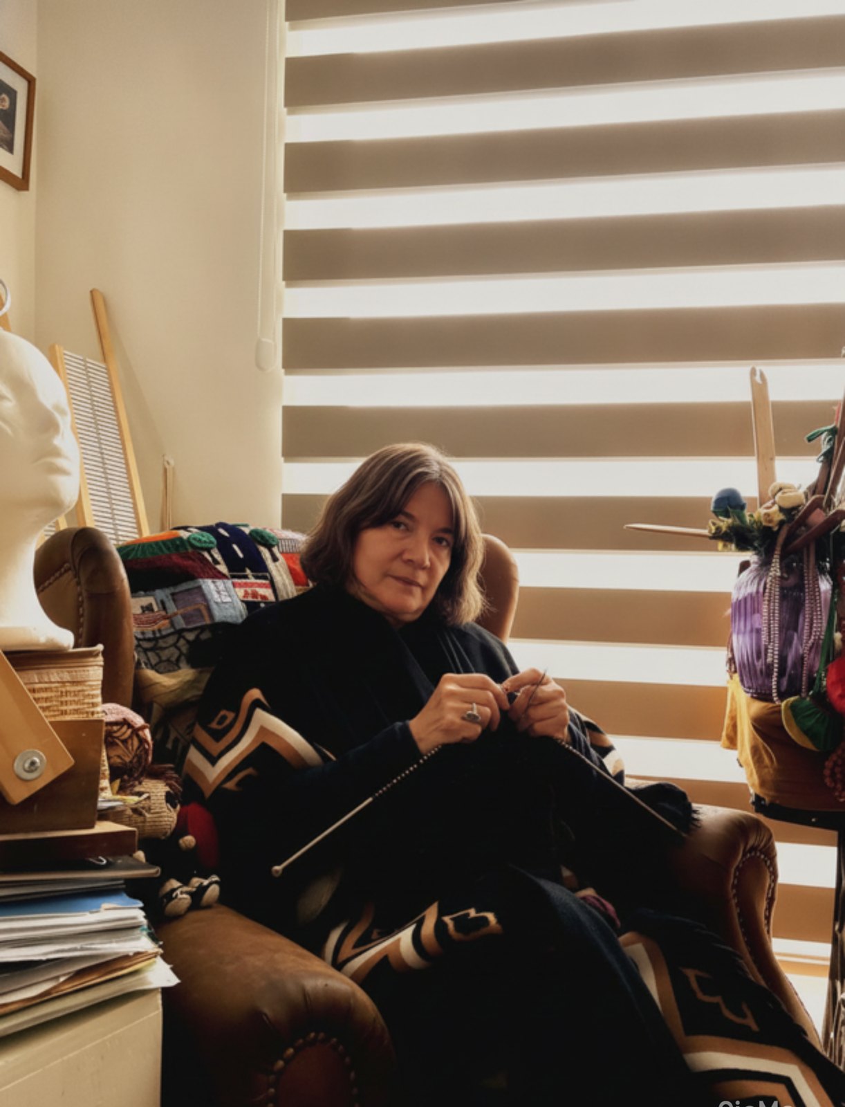 Orietta Romero tejiendo en su sillón, rodeada de sus telares, tocados y piezas